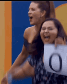 two women are laughing and one is holding a sign that says o