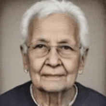 an elderly woman wearing glasses and a blue shirt is smiling for the camera .