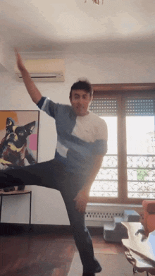 a man is dancing in a living room with a dog painting in the background