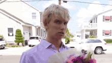 a man in a purple shirt holds a bouquet of pink flowers