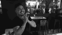 a man with a tattoo on his arm is smiling and clapping in a black and white photo