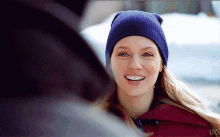 a woman wearing a blue beanie is smiling and looking over her shoulder