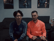two men are sitting on a couch with one wearing a shirt that says ' ata ' on it