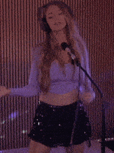 a woman in a purple top and a black skirt is singing into a microphone