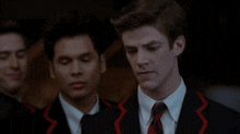 a man in a black suit and red tie stands next to another man