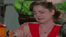 a woman in a red dress is crying in a kitchen while holding an orange pot .