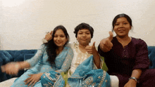 three women are sitting on a couch giving thumbs up