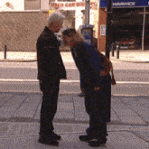 a man and woman are standing on a sidewalk in front of a used car dealership