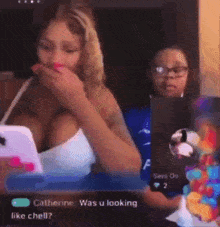 a woman in a white tank top is holding a cell phone while a child looks on