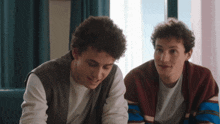 two young men are sitting next to each other looking at something