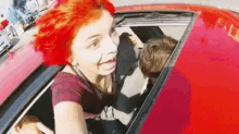 a woman with red hair is sitting in the back seat of a red car with a man .