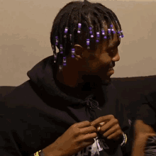 a man with purple beads in his hair is wearing a black hoodie with the letter r on the front