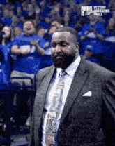 a man in a suit and tie is standing in front of a crowd of people wearing blue shirts .