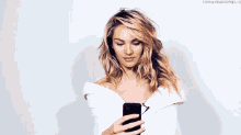 a woman in a white shirt is holding a cell phone in her hand .