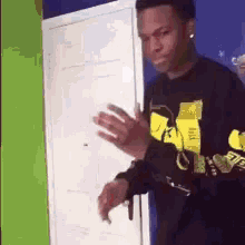 a man wearing a black and yellow shirt is standing in front of a door and smoking a cigarette .