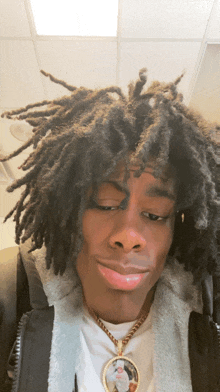 a young man with dreadlocks and a necklace with a picture of jesus on it