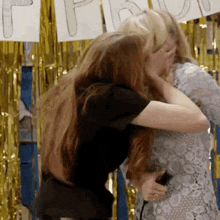 two women hugging each other in front of a sign that says " happy "