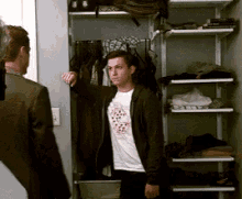 a man in a white shirt is standing in a closet talking to another man