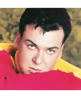 a close up of a man 's face with a pink flower in the foreground