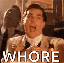 a man in a suit and tie is screaming with his mouth open and the word whore written on his face .