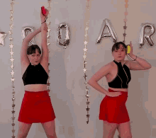 two women in red skirts are dancing in front of a wall that says " dynamite twins " on it
