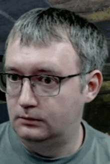 a man wearing glasses and a grey shirt is making a funny face .
