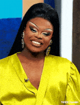 a woman wearing a yellow shirt and earrings smiles for the camera