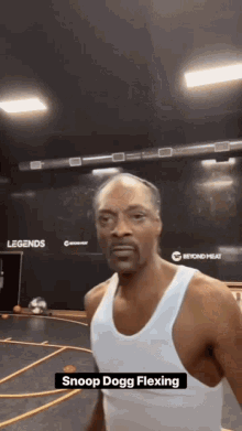 a man in a white tank top is flexing his muscles in a gym