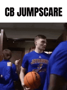a man in a jayhawks shirt is holding a basketball and giving a thumbs up .