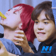 a man with red hair is eating a banana next to another man with a hoodie that says ni nexttide