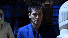 a man in a blue suit stands in front of a white robot