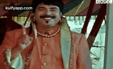 a man with a mustache and a necklace is smiling and giving a thumbs up sign .