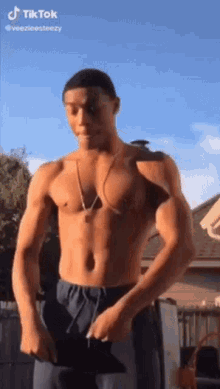 a shirtless man with a necklace around his neck is standing in front of a building .