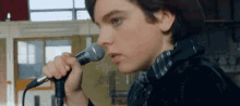 a young man is singing into a microphone while wearing a hat .