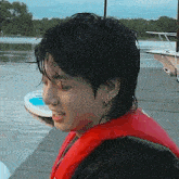 a man in a red life jacket is standing on a dock next to a body of water .