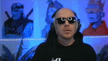 a bald man wearing headphones and sunglasses is standing in front of a painting of a man