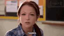 a girl in a plaid shirt is sitting in front of a blackboard and says thanks .