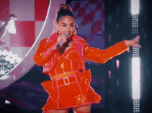 a woman is singing into a microphone in an orange outfit