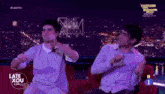 two men are dancing in front of a screen that says late