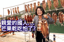 a woman is holding a large fish in front of a bunch of fish hanging on a rack