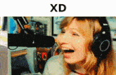 a woman wearing headphones stands in front of a microphone with the word xd below her
