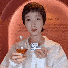 a woman in a white shirt is holding a glass of whiskey and a daily fashion new sign