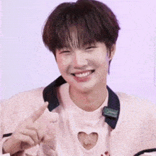 a young man wearing a pink shirt with a heart cut out on it is smiling and pointing at the camera .