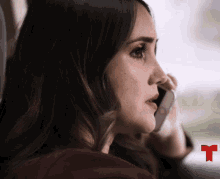 a woman is talking on a cell phone with a red t in the corner