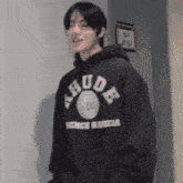 a man wearing a khude hoodie is standing in a hallway .