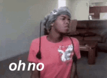 a woman in a pink shirt is standing in a living room with the words oh no written on the screen .