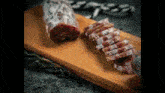a piece of sausage is sitting on a wooden cutting board next to a piece of sausage that has been sliced .