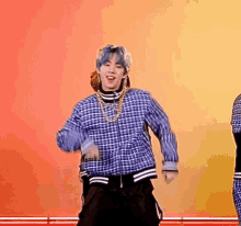 a man with blue hair is dancing on a stage while wearing a plaid shirt .