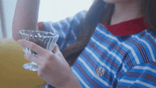 a woman in a blue and red striped shirt is holding a glass in her hand