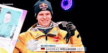 a man wearing a red bull beanie is holding a silver medal